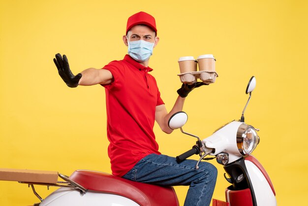 Mensageiro frontal masculino em uniforme vermelho e máscara com café sobre o vírus da pandemia de covidwork de serviço de alimentação de trabalho de cor amarela