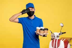 Foto grátis mensageiro masculino com máscara preta segurando café em uniforme amarelo de serviço de cobiçada pandemia de emprego