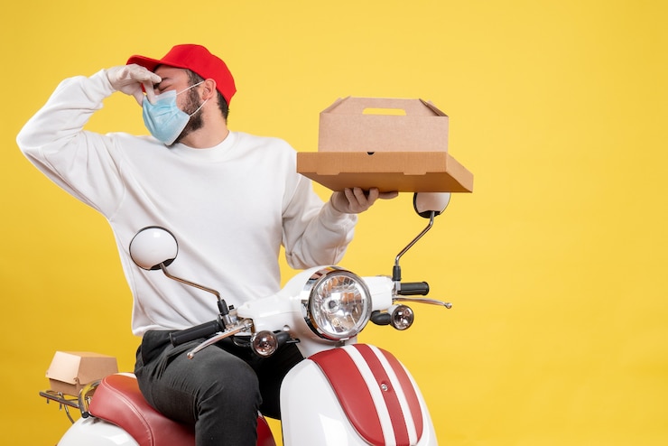 Foto grátis mensageiro masculino com máscara segurando entrega de comida fechando o nariz no amarelo