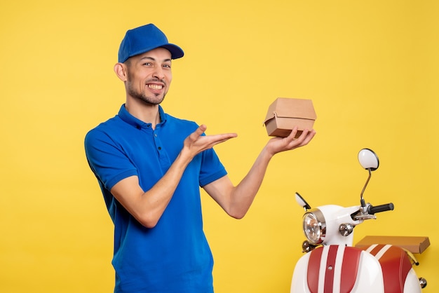 Mensageiro masculino com vista frontal segurando um pequeno pacote de comida em cores amarelas do trabalho serviço trabalho entrega uniforme trabalhador