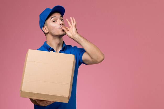 mensageiro masculino de uniforme azul segurando caixa de comida posando na rosa