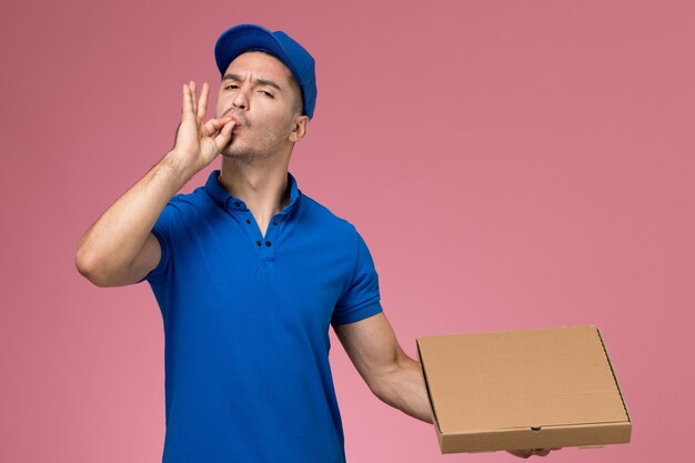 mensageiro masculino de uniforme azul segurando caixa de comida posando na rosa