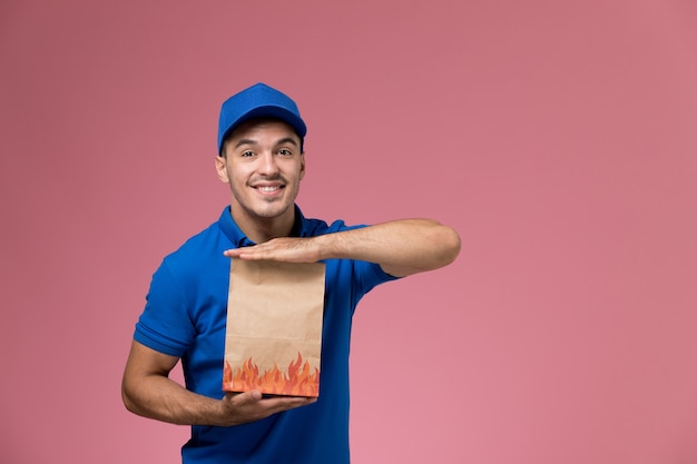 mensageiro masculino de uniforme azul segurando um pacote de comida de entrega sorrindo na rosa, uniforme de trabalhador de trabalho.