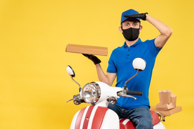 Mensageiro masculino de uniforme azul segurando uma caixa de comida em uma bicicleta pandêmica amarela.