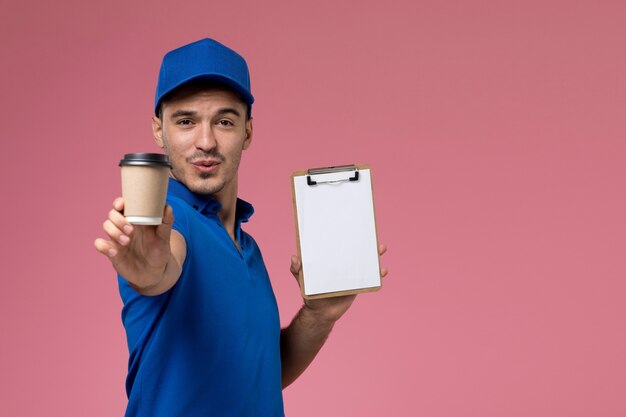 Mensageiro masculino de uniforme azul segurando uma xícara de café marrom com bloco de notas rosa, uniforme de trabalhador.