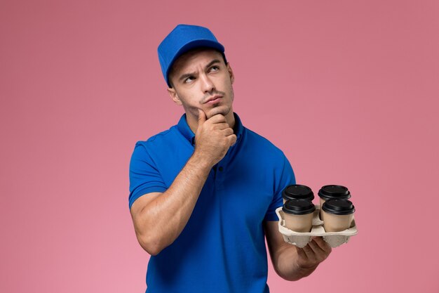 mensageiro masculino de uniforme azul segurando xícaras de café marrom pensando na rosa, entrega de serviço uniforme de trabalhador