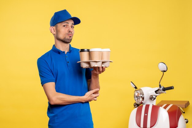 Mensageiro masculino de vista frontal segurando café de entrega em amarelo serviço de cor serviço trabalho de entrega uniforme trabalhador de bicicleta