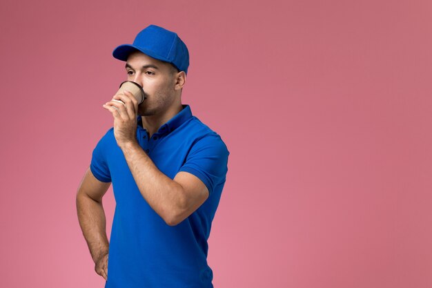 mensageiro masculino em uniforme azul bebendo café rosa, serviço de uniforme de trabalhador