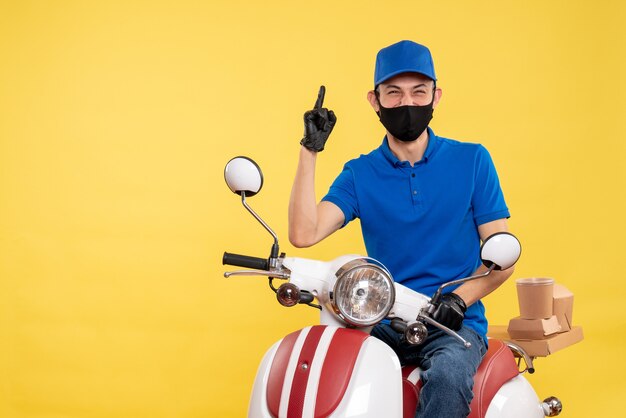 Mensageiro masculino sentado em uma bicicleta, mascarado, com uniforme de serviço secreto de trabalho de entrega de pandemia amarela