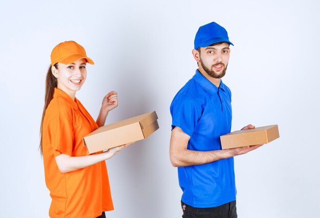 Mensageiro menino e menina em uniformes azuis e amarelos segurando caixas de papelão para viagem e pacotes de compras.