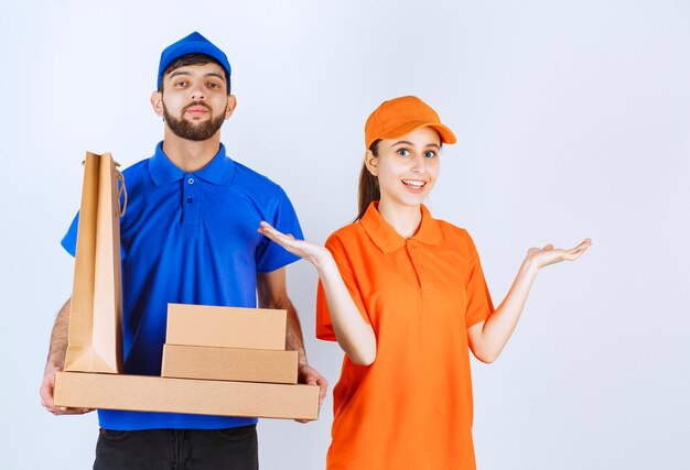 Mensageiro menino e menina em uniformes azuis e amarelos segurando caixas de papelão para viagem e pacotes de compras.