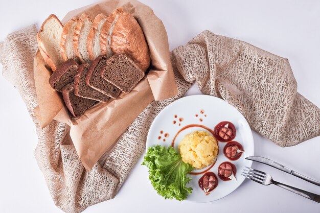 Menu de jantar com linguiça frita, purê de batata e feijão com rodelas de pão.