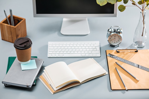 mesa cinza com laptop, bloco de notas com uma folha em branco, vaso de flores, caneta e tablet para retoque