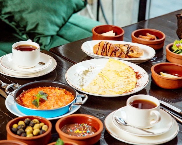 Mesa de café da manhã com xícaras de chá de azeitonas e omelete