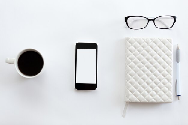 Mesa de escritório branca com óculos, telefone celular, café e caneta