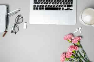 Foto grátis mesa de escritório de mulher plana e leiga espaço de trabalho com artigos de papelaria de cravo rosa para laptop na mesa branca vista superior