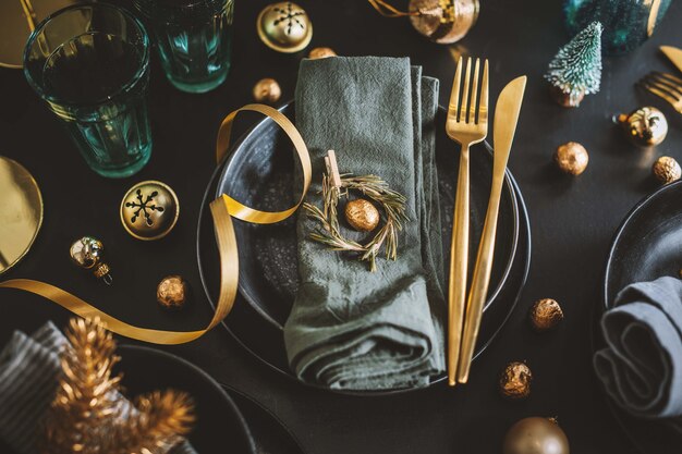 Mesa de Natal servida em tons escuros com decoração dourada.