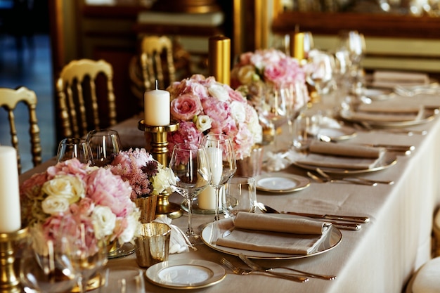 Mesa longa servida com louça de porcelana e talheres brilhantes servidos com flores de cor-de-rosa