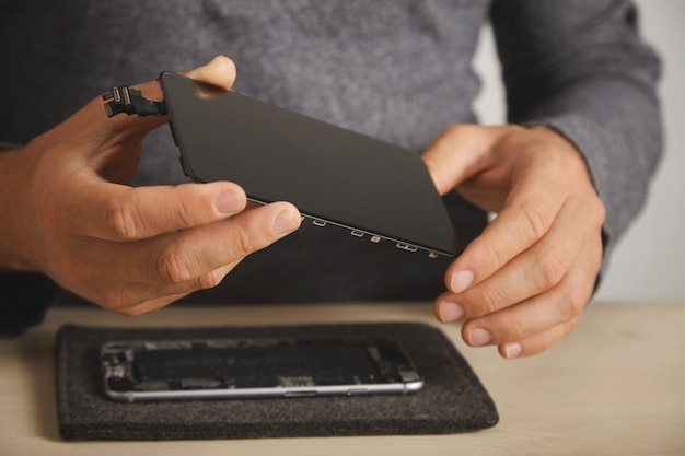 Mestre segura nova tela para substituição acima do smartphone desmontado em seu laboratório, close-up