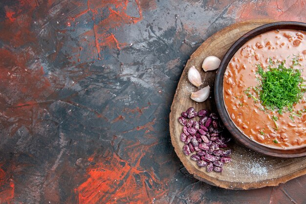 Metade da vista da sopa de tomate com alho e feijão na tábua de madeira na mesa de cores diferentes