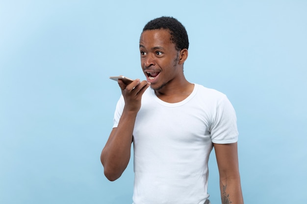 Metade do comprimento fechar o retrato de um jovem afro-americano de camisa branca no espaço azul. emoções humanas, expressão facial, anúncio, conceito