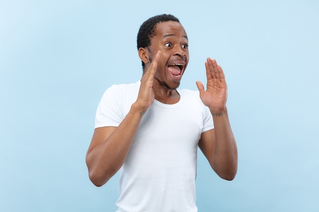 Metade do comprimento fechar o retrato de um jovem afro-americano de camisa branca no espaço azul.