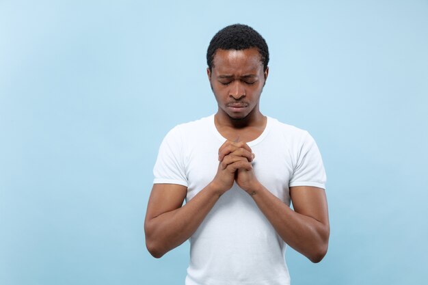 Metade do comprimento fechar o retrato de um jovem afro-americano de camisa branca no espaço azul.