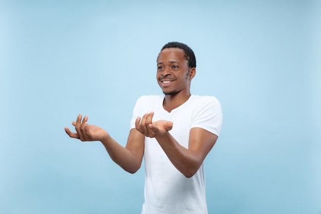 Metade do comprimento fechar o retrato do jovem modelo masculino afro-americano na camisa branca na parede azul. Emoções humanas, expressão facial, conceito de anúncio. Dúvidas, perguntando, mostrando incerteza.