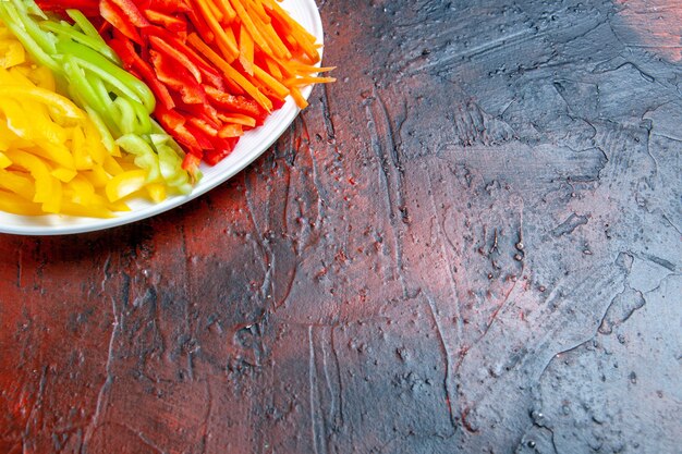 Metade superior vista de pimentas coloridas cortadas em prato branco em mesa vermelho escuro com lugar livre