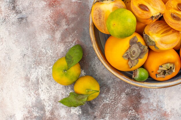 Metade superior vista feykhoas de caquis frescos em uma tigela e tangerinas em um fundo nu