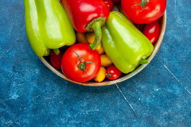 Metade superior vista legumes tomate cereja cores diferentes tomates pimentões em uma tigela na mesa azul