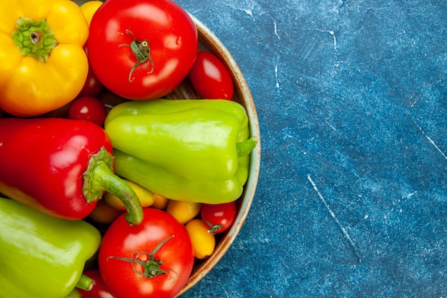 Metade superior vista legumes tomates cereja cores diferentes tomates pimentões em uma bandeja de madeira no lugar da cópia da mesa azul