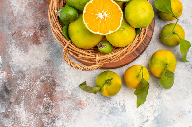 Metade superior vista tangerinas frescas em uma cesta de vime em uma placa de corte em fundo nu