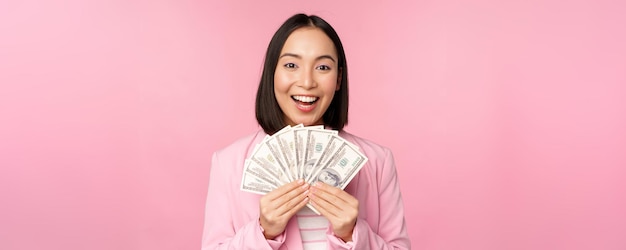 Microcrédito financeiro e conceito de pessoas Feliz empresária asiática sorridente mostrando dinheiro em pé de terno contra fundo rosa