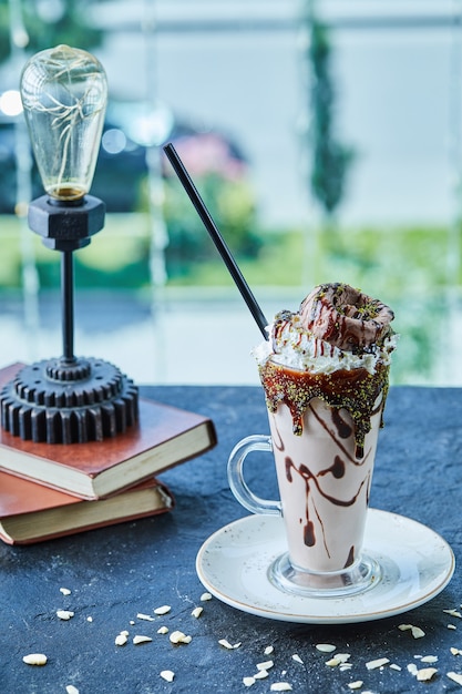 Milkshake com casquinha, chocolate, granulado e livros, abajur na superfície escura