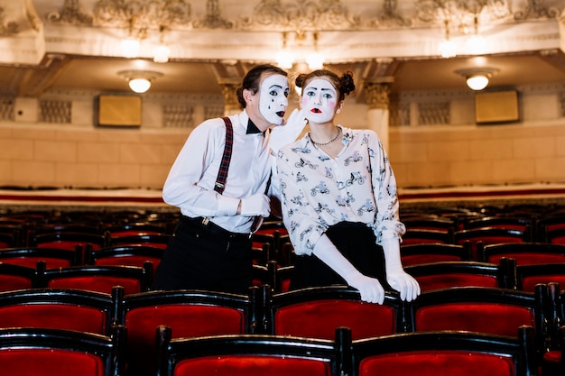 Foto grátis mime masculino sussurrando no ouvido do mime feminino em pé entre a cadeira