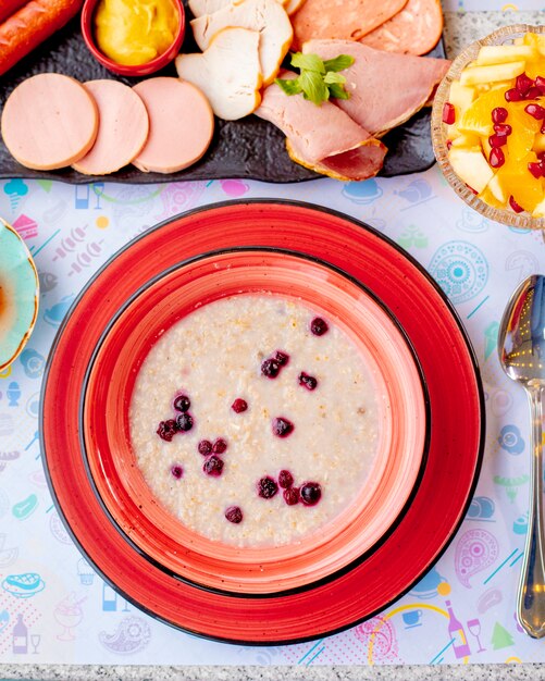 Mingau de aveia com frutas e prato de carne em cima da mesa