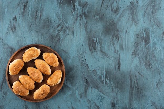 Foto grátis mini croissants doces em uma placa de madeira sobre uma superfície azul escura