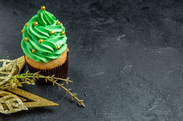 Mini cupcake da árvore de natal com vista de cima e enfeite dourado pendurado em fundo escuro.