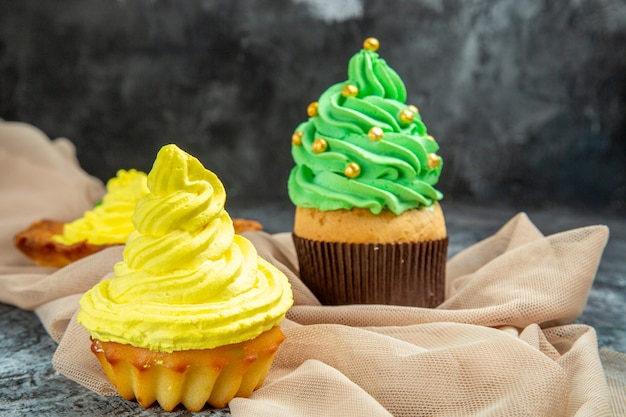 Mini cupcakes coloridos de frente e xale bege de biscoito no escuro