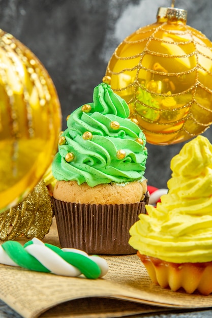 Mini cupcakes coloridos de frente para a árvore de natal brinquedos doces de natal no jornal na foto de ano novo escuro