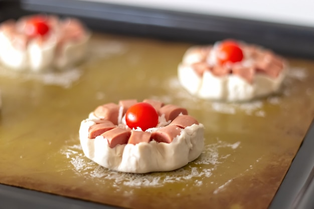 Mini torta de massa folhada crua com linguiça e tomate cereja pronta para assar. foco seletivo. Foto Premium