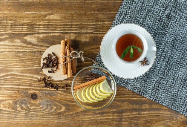Minty chá com biscoitos, cravo, rodelas de limão, paus de canela em um copo na superfície de madeira