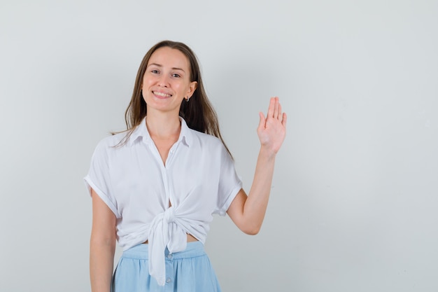 Moça acenando com a mão para se despedir de blusa e saia e parecendo feliz