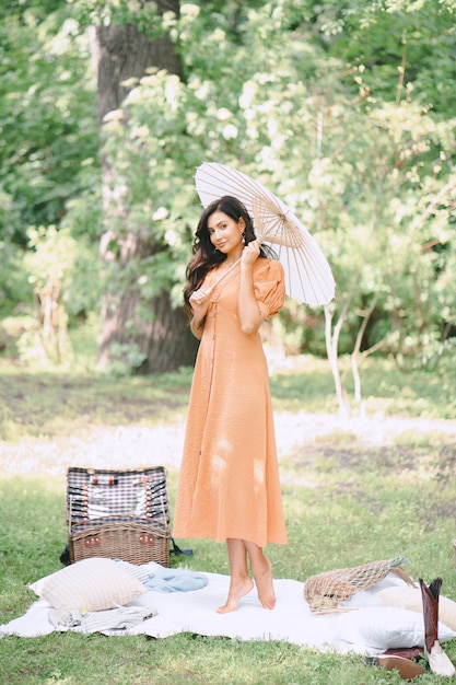 Moça bonita, segurando o guarda-chuva e olhando no vestido laranja na natureza durante o dia.