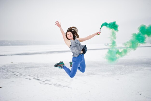 Moça com bomba de fumaça de cor verde à disposição no dia de inverno