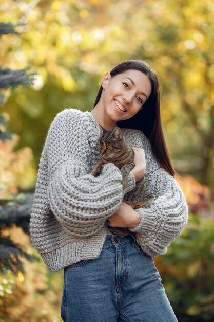 Moça em um suéter cinza posando ao ar livre com um gato