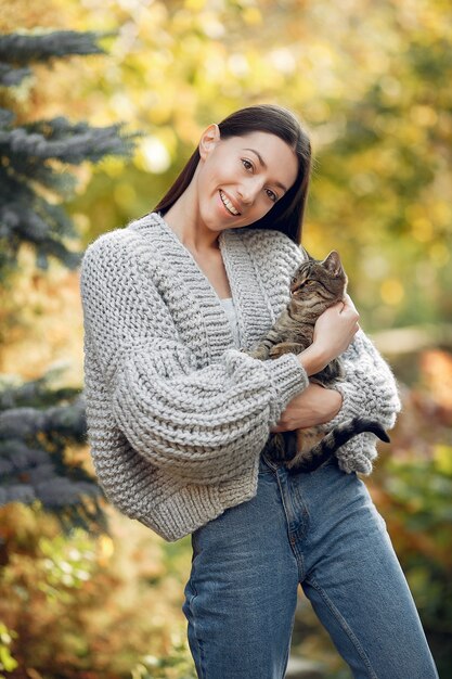 Moça em um suéter cinza posando ao ar livre com um gato