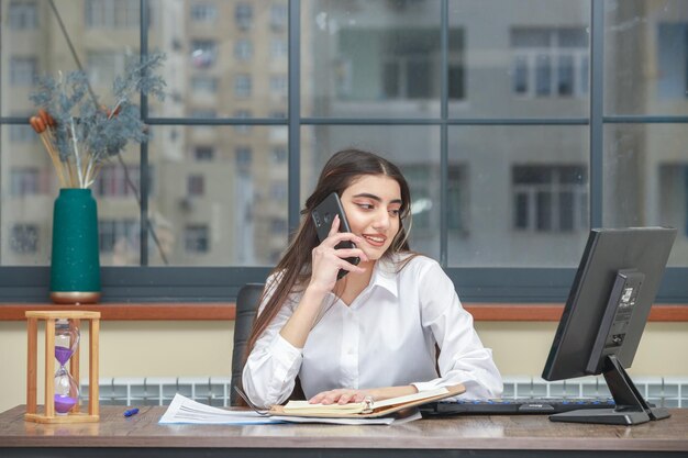 Moça falando ao telefone e olhando para o pc