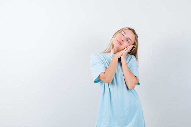 Moça fazendo travesseiro no rosto com as mãos em uma camiseta e parecendo com sono isolada